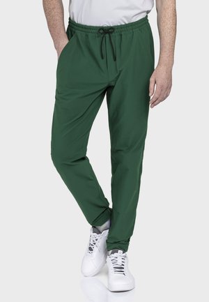 Grüne Jogginghosen aus leichtem Stoff, mit elastischem Bund und Kordelzug sowie Seitentaschen. Kombiniert mit weißen Sneakern.