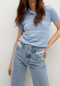 Polo shirt tricoté bleu clair à manches courtes et col côtelé, associé à un jean en denim bleu clair taille haute avec des détails de poches.