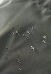 Des gouttes d'eau perlent sur un tissu lisse gris foncé, indiquant une surface hydrofuge ou imperméable.