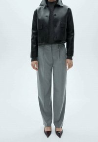 Personne portant une veste en cuir noire courte, un pull en maille gris foncé, un pantalon sur mesure gris clair et des chaussures à bout pointu marron foncé.