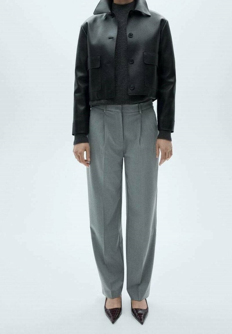 Personne portant une veste en cuir noire courte, un pull en maille gris foncé, un pantalon sur mesure gris clair et des chaussures à bout pointu marron foncé.