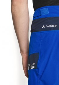 Siniset ulkoilushortsit, joissa on tummansiniset vyötärönauhat, sivutasku ja logo. Materiaali näyttää kevyeltä ja sileältä.