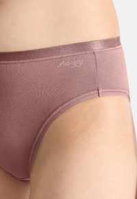 Slip da donna rosa chiaro con una texture liscia e una fascia in vita senza cuciture; design minimalista con un piccolo logo sul lato.