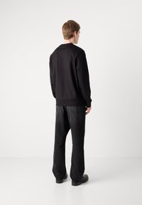 Sweatshirt preto com decote redondo, combinado com jeans pretos de corte solto. Textura de tecido suave e design minimalista. Simples e monocromático.