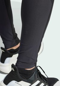 Leggings deportivos negros con un acabado texturizado, con costuras en contraste. Combinados con zapatillas de running en negro y blanco etiquetadas como "ULTRABOOST".