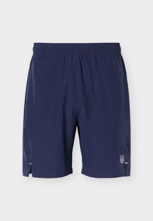 Αθλητικό σορτς σε ναυτικό μπλε με ελαστική μέση, μικρές πλαϊνές σχισμές και αντανακλαστικό λογότυπο ασπίδας κοντά στο κάτω ρεβέρ του δεξιού ποδιού.