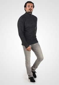 Suéter de cuello alto gris oscuro con un tejido texturizado, combinado con jeans gris claro y zapatillas negras con un acento beige.