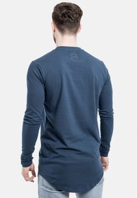 Langærmet navy blå T-shirt lavet af blødt stof, med en rund halsudskæring og buet kant, og med et diskret logo broderet på ryggen.