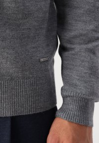 Šedý pletený svetr s žebrovanými manžetami a lemem. Na spodním okraji se nachází malý kovový štítek s nápisem "JOOP!". Měkká textura, ležérní design.