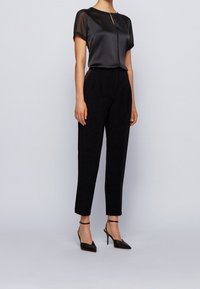 Svart silkig kortärmad topp med en nyckelhålsdetalj, matchad med högmidjade, skräddarsydda svarta byxor och svarta remsandaler.