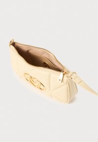 Κρεμ τσάντα με ραμμένο σχέδιο, με χρυσό λογότυπο, κλείσιμο με φερμουάρ και αποσπώμενο ιμάντα. Μαλακό υλικό με λεία υφή.