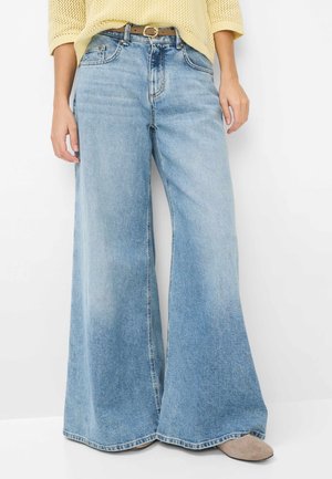 Jeans a gamba larga color azzurro chiaro con vita alta e cintura marrone, indossati con un maglione a maglia giallo pallido e scarpe beige.