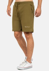 Shorts verde oliva con coulisse realizzati in tessuto misto cotone, caratterizzati da tasche laterali e un logo bianco discreto sulla gamba sinistra.