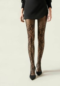 Medias de encaje negro con patrón floral y diseño de red, combinadas con una falda corta negra y tacones negros puntiagudos.