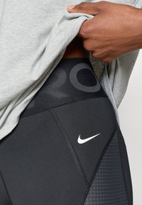 Schwarze sportliche Leggings mit einem strukturierten Seitenpaneel, das einen großen "PRO"-Druck am Bund und ein kleines weißes Nike-Logo aufweist.