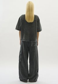 Grå denimoutfit som består av en kortärmad topp med synliga sömmar och vida byxor med cargofickor och broderade detaljer.