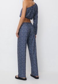 Modrý květinový dvoudílný outfit, který obsahuje zkrácený top s volnými ramínky a široké kalhoty. Materiál se zdá být lehký a má uvolněný střih.