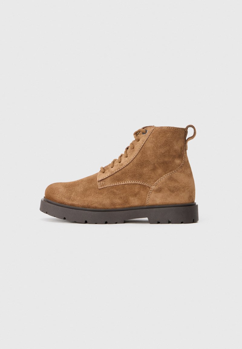Botas de tobillo de ante marrón con punta redondeada, cordones en la parte frontal y una suela de goma resistente que presenta detalles de tracción y una pestaña en el talón.