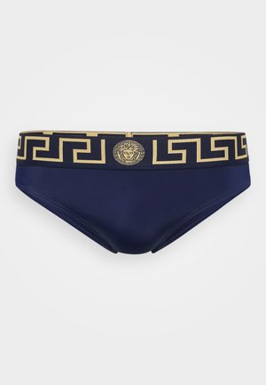 Jūras tumši zili peldbikses ar zelta ģeometrisku rakstu vidukļa joslā, kas priekšā izceļ centrālo medaljonu. Gluda, elastīga auduma.