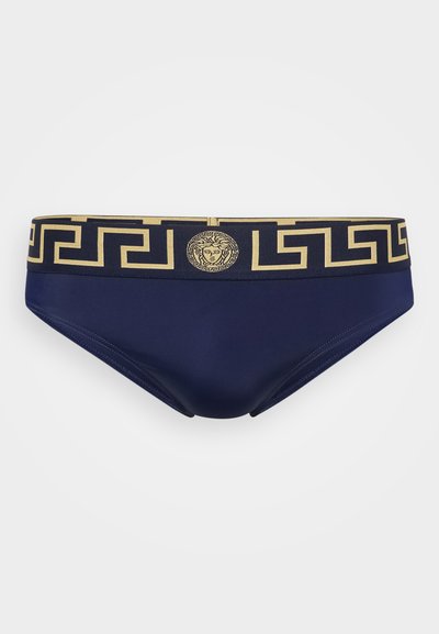 Jūras tumši zili peldbikses ar zelta ģeometrisku rakstu vidukļa joslā, kas priekšā izceļ centrālo medaljonu. Gluda, elastīga auduma.