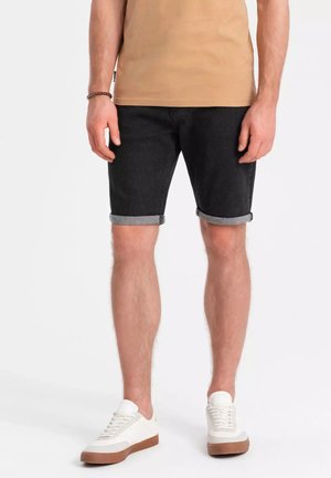Shorts en denim noir avec des ourlets retroussés, associés à un t-shirt beige et des baskets blanches avec des semelles marron. La texture est lisse et décontractée.