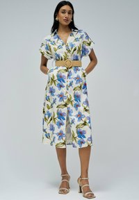 Vestido midi floral en blanco, con flores azules y naranjas, mangas cortas, frente de botones y un cinturón trenzado beige en la cintura.