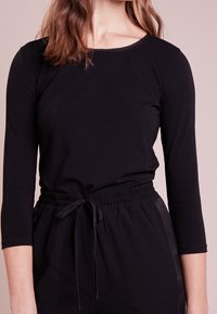 Schwarzes Langarmoberteil mit Rundhalsausschnitt, aus weichem Stoff, kombiniert mit schwarzen Hosen mit elastischem Bund und verstellbarem Kordelzug.