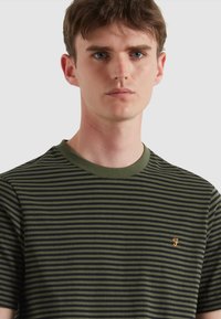 Camiseta de rayas en algodón negro y verde oscuro, con escote redondo y un logo bordado en dorado en el pecho.