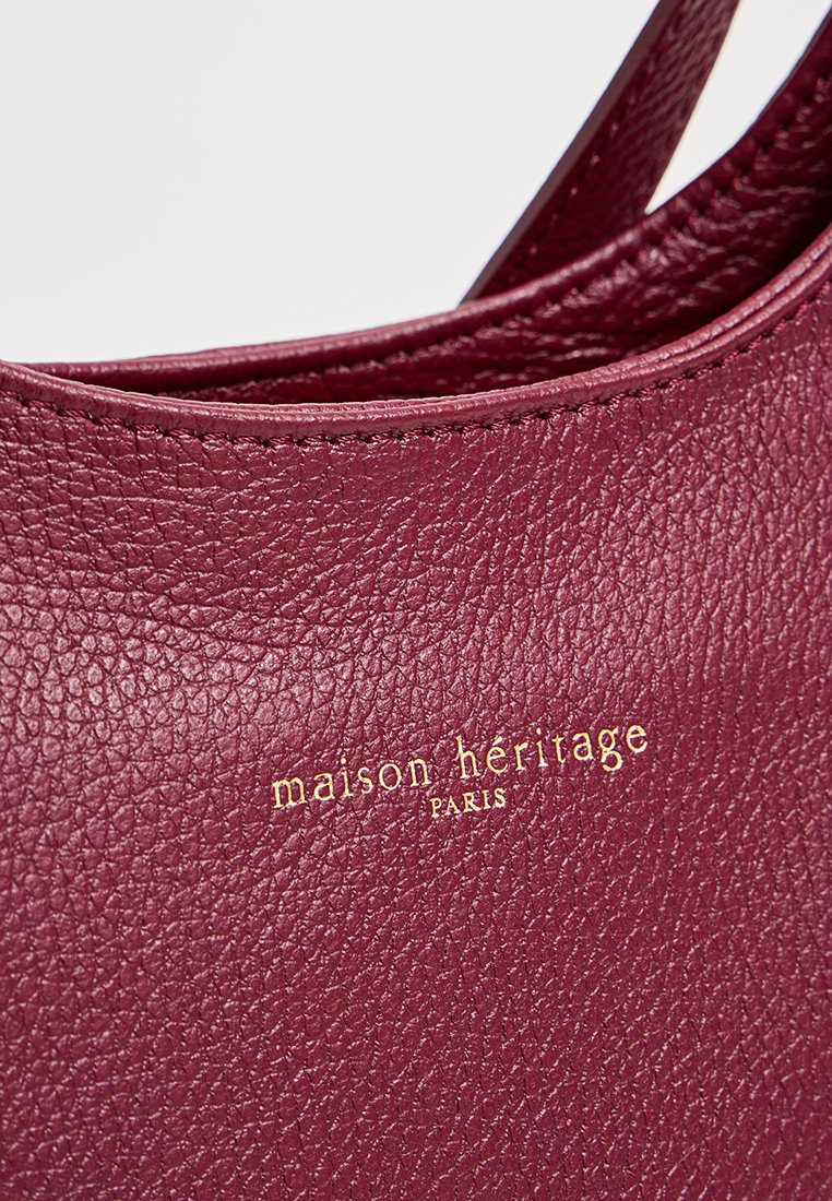 Sac à main en cuir bordeaux avec une surface texturée, arborant une lettrage doré en relief qui indique "maison héritage PARIS."