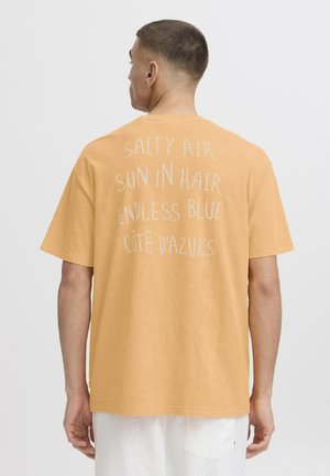 Short-sleeve, loose-fitting t-shirt in soft, mustard yellow fabric. Features white text on the back: "SALTY AIR, SUN IN HAIR, ENDLESS BLUE CÔTE D'AZURS."