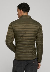 Olivgrüne Steppjacke mit gesteppter Optik, hohem Kragen und elastischen Bündchen, aus leichtem, wasserabweisendem Material gefertigt.