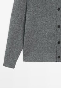 Manica e parte anteriore inferiore di un cardigan grigio lavorato a maglia con bottoni neri su uno sfondo bianco.