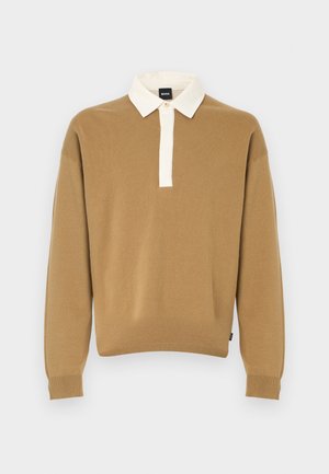 Brun strikket genser med en hvit, brettet krage og en kort knappet slisse. Har lange ermer og ribbestrikkede mansjetter.