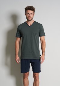 Tricou verde cu decolteu în V, cu mâneci scurte și un accent bleumarin la gât, asortat cu șorturi bleumarin. Textură fină, design lejer.