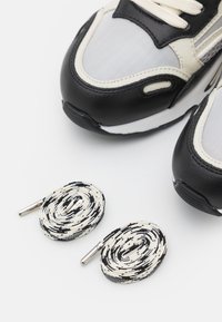 Pari di scarpe da ginnastica bianche e nere con lacci a spirale abbinati in bianco e nero su uno sfondo bianco.