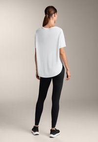 Bílý krátký rukáv s kulatým lemem, kombinovaný s černými legínami a černými sportovními botami. Hladká látka s volným střihem.