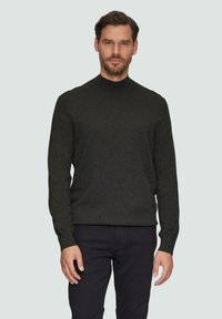 Donkergroene gebreide trui met een hoge hals, lange mouwen en een aansluitende silhouet, gecombineerd met zwarte broek. Gladde textuur, minimale details.