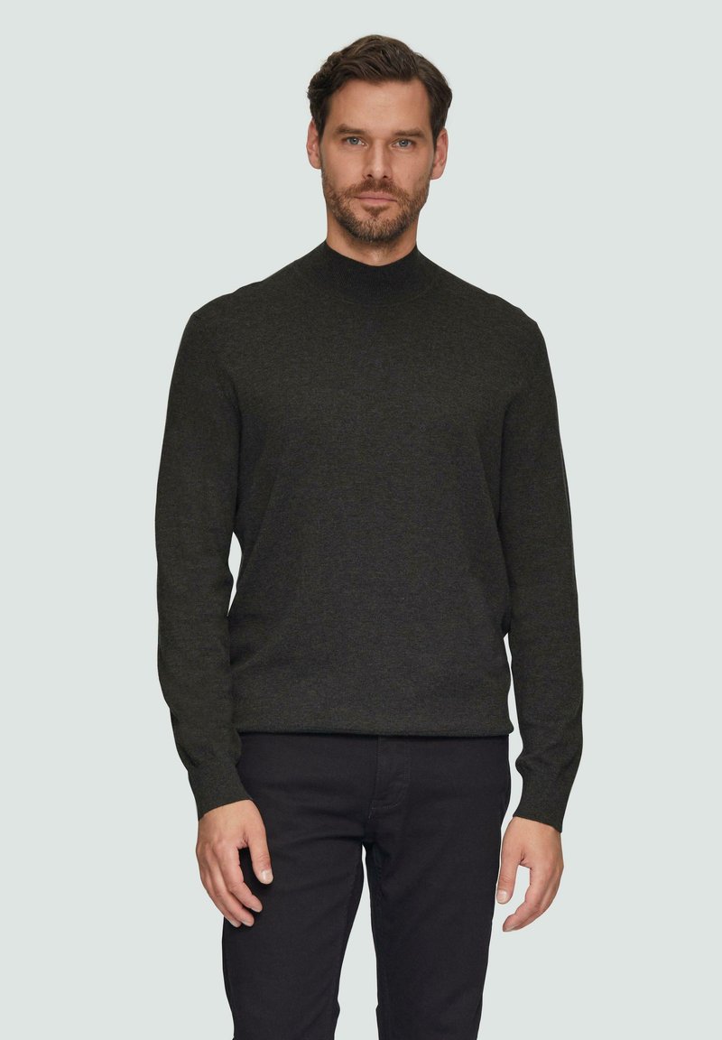 Donkergroene gebreide trui met een hoge hals, lange mouwen en een aansluitende silhouet, gecombineerd met zwarte broek. Gladde textuur, minimale details.