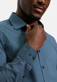 Hemd mit Knöpfen in Dunkelblau mit einem geometrischen weißen Muster. Verfügt über einen strukturierten Kragen und Manschetten mit dunklen Knöpfen zum Schließen.