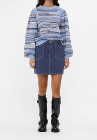 Niebiesko-kremowy sweter w paski z dzianiny z bufkami na rękawach, zestawiony z granatową spódnicą dżinsową z przednimi kieszeniami i kontrastowym przeszyciem, noszony z czarnymi kozakami za kolano.