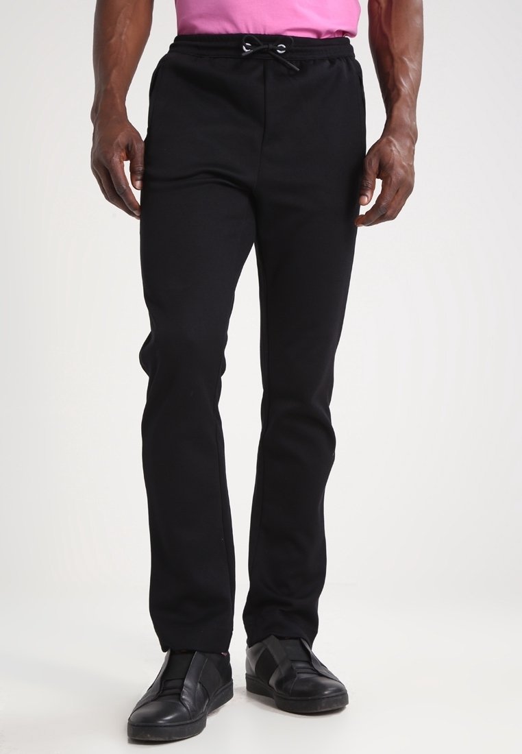 Czarne spodnie dresowe z regulowanym pasem na sznurek, dopasowanym krojem i gładką fakturą. Uzupełnione czarnymi trampkami z wzorem plecionym.
