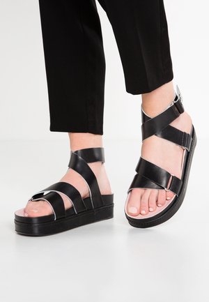 Black leather platform sandals with wide straps, silver accents, and a rounded toe design. Features adjustable buckle for secure fit.