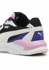 La sneaker PUMA presenta una toma superior in rete nera, sovrapposizioni sintetiche bianche e viola, e un accento rosa in gomma sul tallone. Suola spessa bianca.