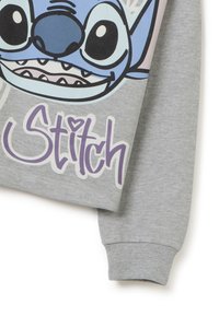 Grijze sweatshirt met het gezicht van een blauwe tekenfilmfiguur en het woord "Stitch" in paarse letters. Boordjes aan de mouwen en zachte stof.