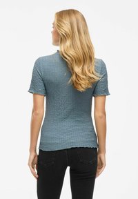 Top corto a maniche corte in un morbido blu, con orlo scallop, caratterizzato da una silhouette aderente e un design di tessuto leggermente arricciato.