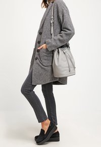 Šedý vlněný kabát s velkými knoflíky, šedá kabela typu bucket, tmavé úzké džíny a černé slip-on boty. Čisté linie a strukturované materiály.