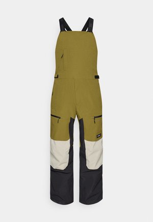 Pantalones de peto impermeables en verde oliva con piernas en bloques de color negro y crema. Cuenta con tirantes ajustables y bolsillos con cremallera.