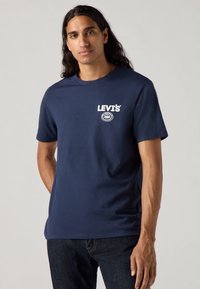 Jūras zila kokvilnas t-kreklu ar apļveida kakla izgriezumu, ar baltu LEVI'S logotipu un apļa grafiku kreisajā krūtīs. Īsas piedurknes, gluda tekstūra.