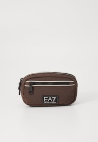 Καφέ νάιλον θήκη με φερμουάρ και λευκές διακοσμητικές ρίγες, διαθέτοντας ένα μαύρο λογότυπο EA7 στο μπροστινό μέρος. Συμπαγής και στρογγυλή σχεδίαση.