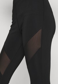 Svarta leggings med en åtsittande design, nätpaneler på sidorna, en mjuk textur och kontrasterande sömmar för extra detalj.